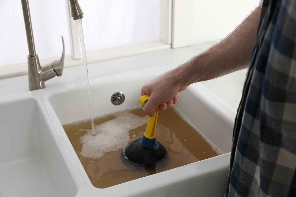 man using plunger to unclog sink drain