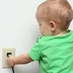 young child touching a power outlet and cord